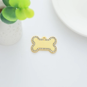 Golden bone-shaped pet ID tag with rhinestones on white background with green plants