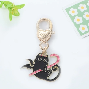 Détail d'un porte-clés chat noir avec ailes et sucette rose sur fermoir cœur doré