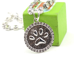 Macro view of a silver pet pendant with a dark paw print and sparkling crystal trim