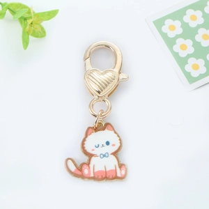Detail of cute enamel cat keychain with heart-shaped golden clasp and blue bow decor