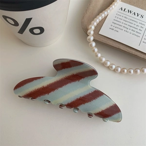 Close-up of a blue and brown plaid acetate hair claw clip beside a coffee cup and pearls