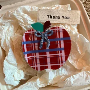 Close-up of apple-shaped hair claw clip with red and blue plaid pattern in a gift box