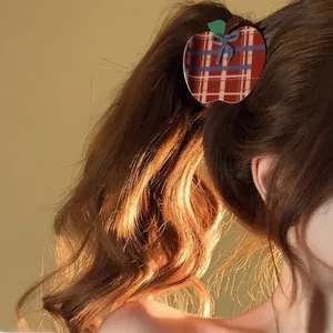 Detail view of a plaid apple hair claw clip with a blue bow on a high ponytail