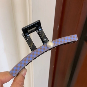 Close-up of a large black hair claw clip featuring blue argyle pattern and a center pearl