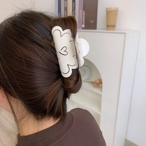 Détail d'une pince à cheveux crème avec motif cœur portée sur cheveux châtains