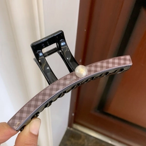 Detail of a large checkerboard hair claw clip with a glossy finish and white pearl accent