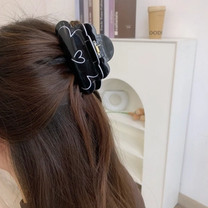 Détail d'une pince à cheveux noire à motif coeur blanc sur des cheveux bruns