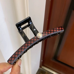 Detail view of large checkered hair claw clip with pearl accent on polished black finish