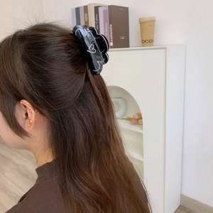 Détail d'une pince à cheveux noire à motif cœur portée sur un mannequin aux cheveux bruns