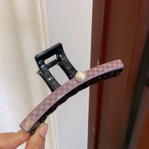 Detail of a black PVC hair claw clip featuring a pink checkered pattern and a faux pearl accent