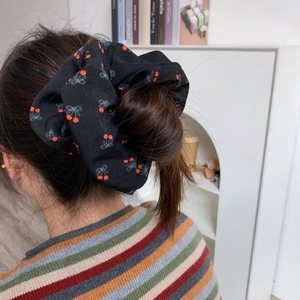 Détail d'un grand chouchou noir avec cerises et nœuds bleus sur une queue de cheval