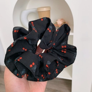 Gros plan d'un chouchou en mousseline noire avec des motifs de cerises rouges et nœuds bleus