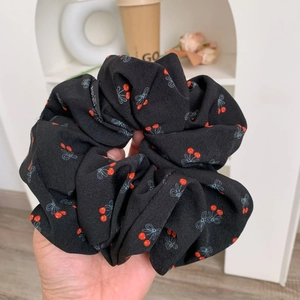 Détail d'un chouchou en tissu noir avec des motifs de cerises et de nœuds