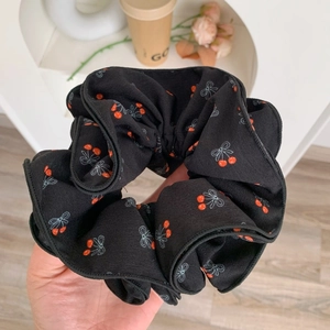 Vue détaillée du chouchou noir avec de jolis motifs de cerises rouges et de nœuds bleus