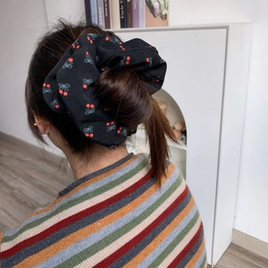 Détail d'un chouchou noir avec motifs cerises et nœuds sur une queue de cheval
