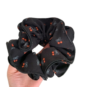 Chouchou noir avec motifs de cerises rouges tenu à la main sur un fond blanc épuré