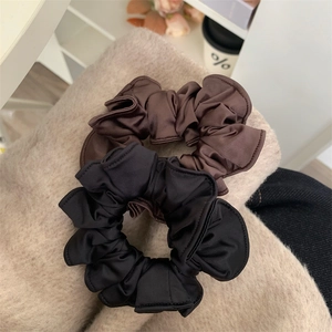 Elegant large satin scrunchies in black and brown on a soft aesthetic fabric background