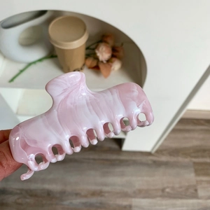 Close-up of a pink and white marble texture acetate shark hair claw clip in hand