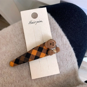 Détail d'une barrette à cheveux à carreaux ornée d'un petit ours en peluche marron