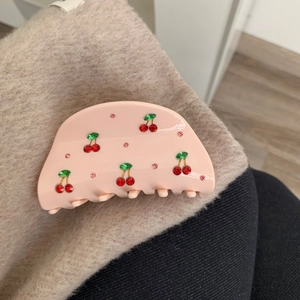 Détail d'une pince à cheveux rose en acétate avec motif cerise en strass brillants