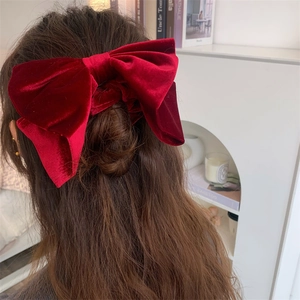 Détail d'un grand chouchou nœud en velours bordeaux porté sur des cheveux longs et ondulés