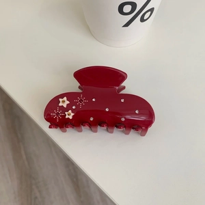 Close-up of a burgundy acetate shark hair claw clip with star patterns and sparkling rhinestones