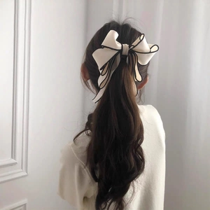 Elegant cream fabric bow hair clip with black piping shown on a ponytail hairstyle