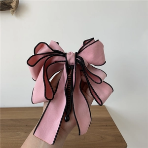 Close-up of pink layered fabric bow hair clip with black edges held in hand
