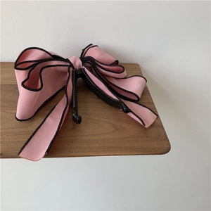 Detail view of pink satin bow hair clip with black wavy edges on a wooden shelf
