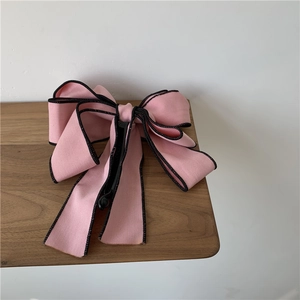 Detailed view of pink fabric bow hair clip with black wavy edge on natural wood desk