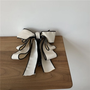 Close-up of elegant cream bow hair claw clip with black piping on rustic wooden table