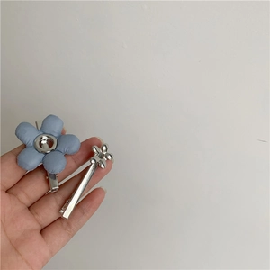 Hand met set van 2 hemelblauwe stoffen bloemen en zilveren metalen haarspelden voor meisjes