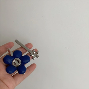 Detail van twee metalen haarspeldjes met donkerblauwe stoffen en zilveren bloemen