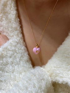 Gros plan d'un pendentif cœur en émail rose doux sur une fine chaîne dorée élégante