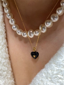Détail d'un collier doré avec pendentif cœur en émail noir et perles blanches