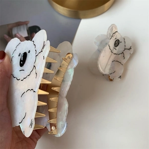 Detail of koala-shaped acetate hair claw clip with white pearl finish and golden metal teeth