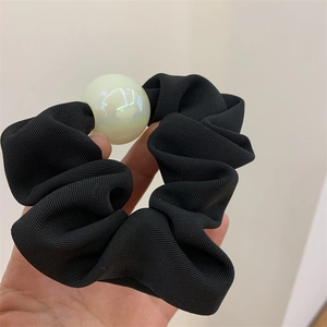 Detail eines schwarzen Scrunchies mit großer irisierender Perle und Stofftextur