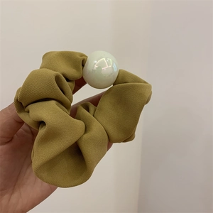 Detail eines senfgelben Scrunchies aus strukturiertem Stoff mit einer großen glänzenden Perle