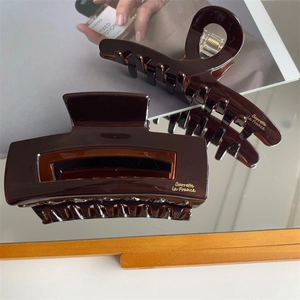 Detailed view of dark brown acetate hair claw clips with elegant golden brand lettering