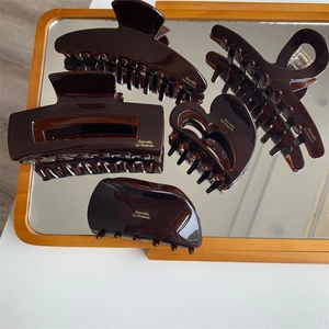 Detail of five dark amber acetate hair claws with gold logo lettering on mirror surface