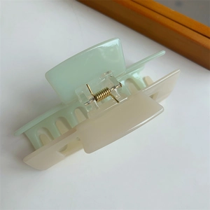 Detail of a rectangular two-tone hair claw clip in light green and cream with gold spring