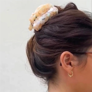 Detail view of a tortoiseshell acetate hair claw clip on a woman's hair with marble texture