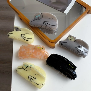 Various colors of cat-shaped acetate hair claws displayed near a mirror and books