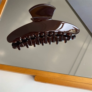 Macro shot of large chocolate acetate hair claw with gold logo and smooth mirror finish