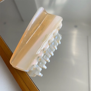 Vue détaillée d'une pince à cheveux en acétate beige champagne avec lettrage doré sur miroir