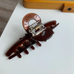 Detail of a brown acetate hair claw clip showing a semi-circular design and gold spring