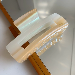 Détail d'une pince à cheveux en acétate crème avec lettrage doré et texture nacrée