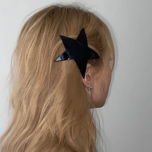 Detail of a black star hair clip with logo engraving styled on long blonde hair