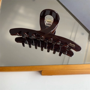Detail showing the polished dark brown acetate hair claw with gold logo text