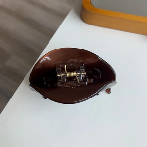 Detailed close-up of dark brown hair claw clip with golden metal spring mechanism